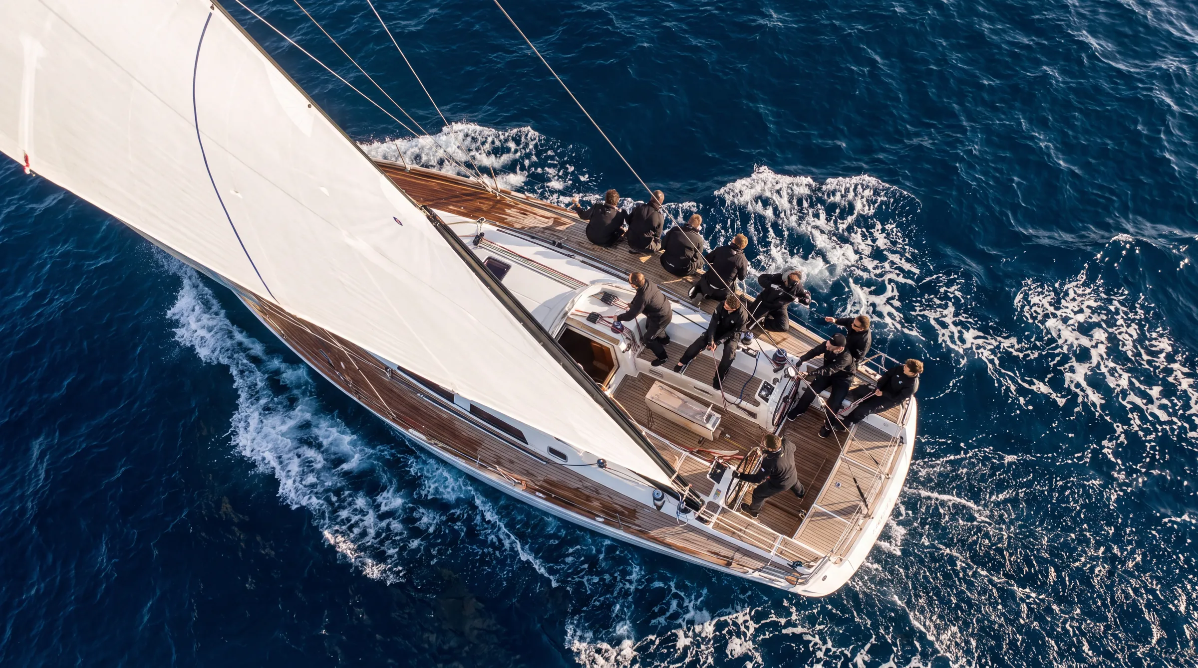 A racing yacht crew tacking in sync on deep blue water, seen from above