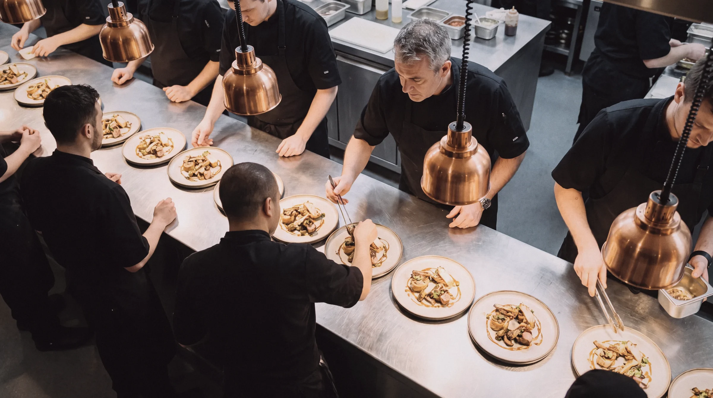 A fine-dining kitchen pass from above, chefs plating in a line
