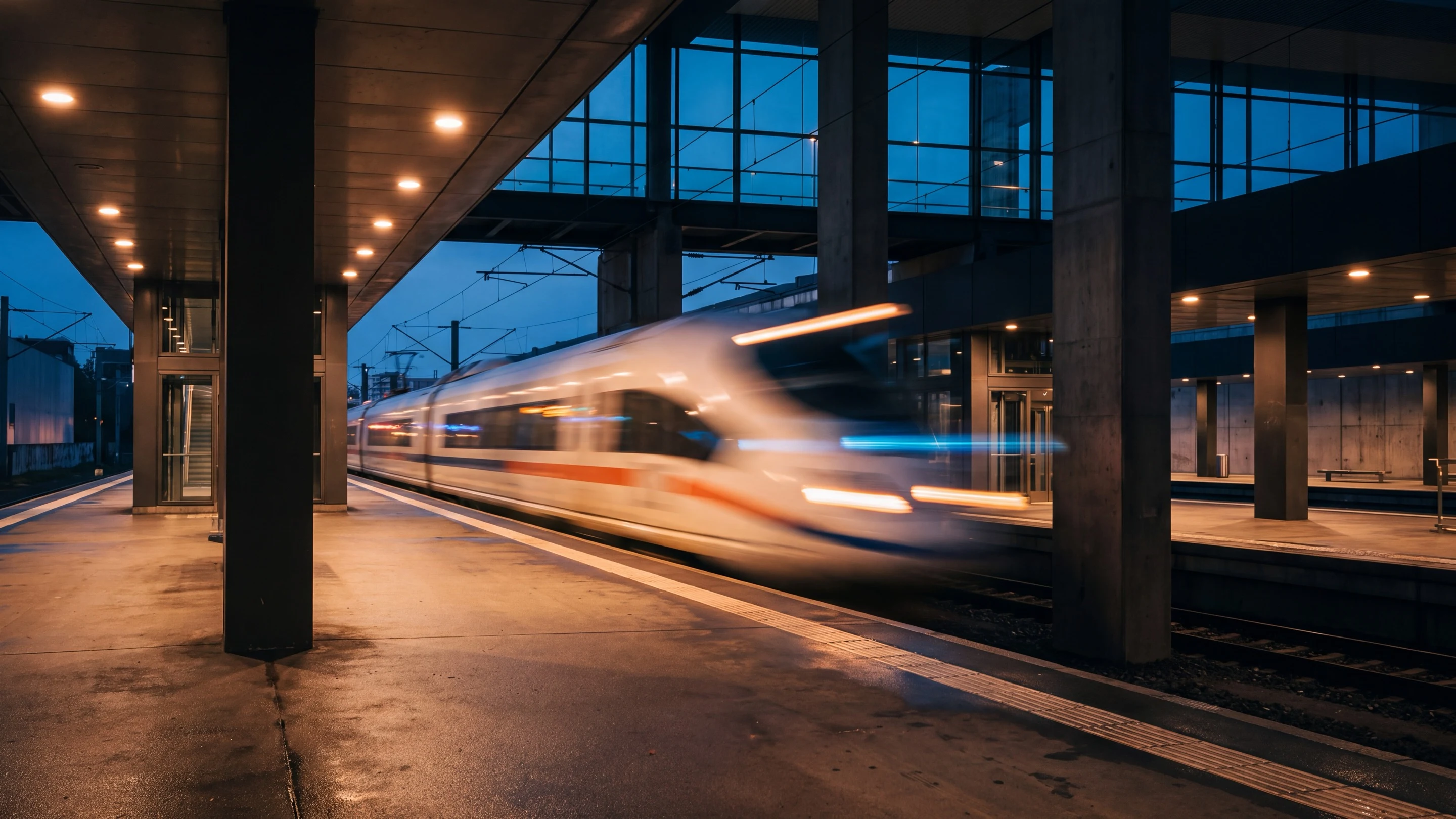 A high-speed train streaking past a still platform at dusk